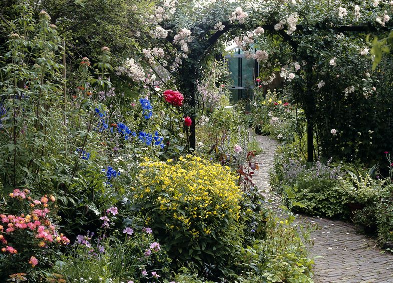 Rosenbogen über einem Gartenweg, rundherum üppige Beete