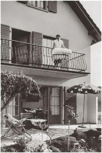 Schwarz-Weiß-Foto eines Einfamilienhauses mit Frau auf dem Balkon und Mann im Gartenstuhl