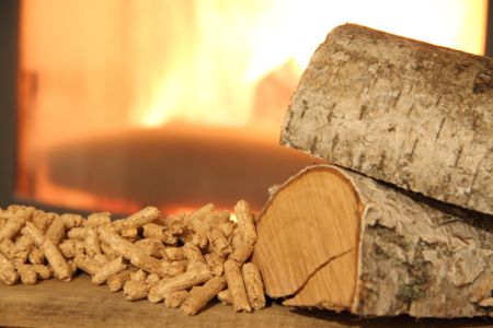 Ein Haufen Holzpellets und Holzscheite liegen vor einem brennenden Kamin.