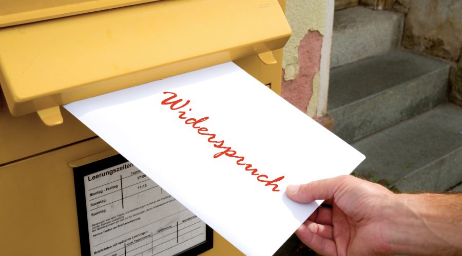 Brief mit dem Wort Widerspruch, der in einen gelben Briefkasten eingeworfen wird.