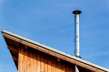 Ein Holzhaus mit einem modernen Edelstahlkamin, der durch das Dach ragt.