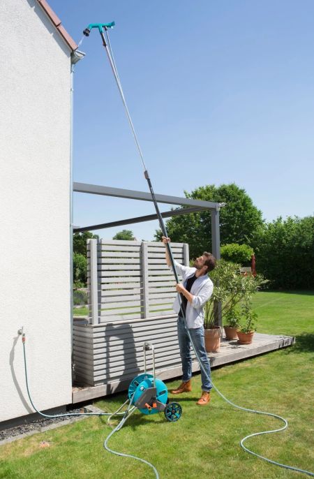 Ein Mann reinigt eine hohe Hausfassade mit einem langen Teleskop-Wasserbesen.