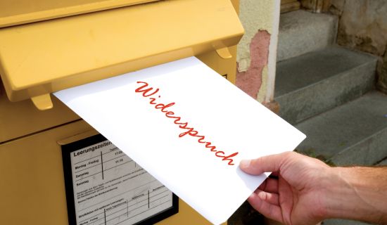 Brief mit dem Wort Widerspruch, der in einen gelben Briefkasten eingeworfen wird.