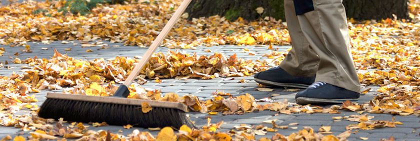 Mann fegt Herbstlaub zusammen