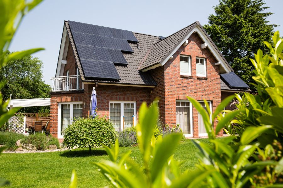 Ein modernes Einfamilienhaus mit rotem Ziegelstein, Solarzellen auf dem Dach und einem gepflegten Garten im Vordergrund.