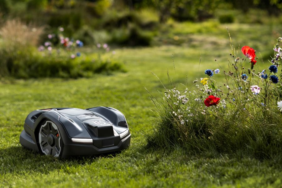 Ein autonomer Mähroboter auf einer Wiese, umgeben von bunten Blumen im Hintergrund.