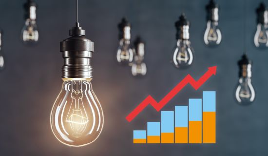 Das Bild zeigt eine leuchtende Glühbirne im Vordergrund, umgeben von weiteren Glühbirnen im Hintergrund, sowie einem Diagramm mit aufsteigenden Balken in Blau und Orange und einem roten Pfeil, der den Wachstumstrend symbolisiert.
